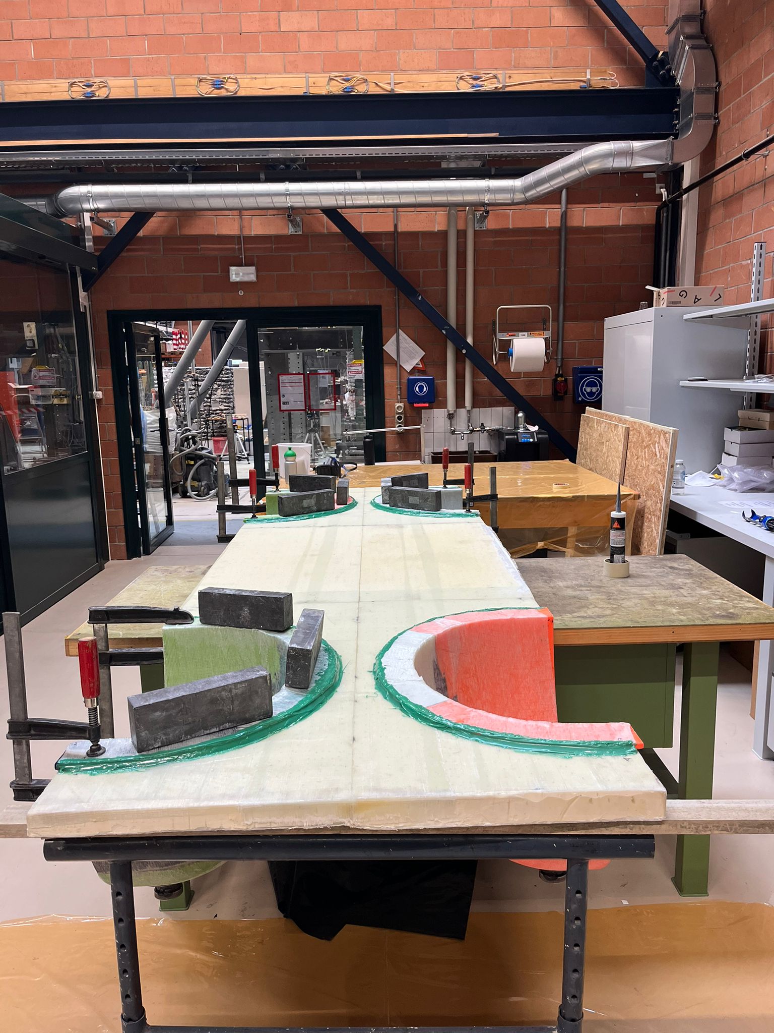 The composite plate on trestles with eggshells bonded into its cutouts, held by steel weights and clamps, green epoxy fillets at the joints
